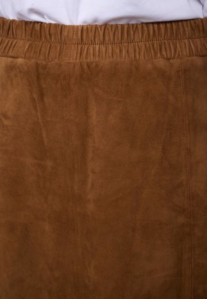 Brown suede skirt with elastic waistband worn over a white top, showing texture and stitching details.