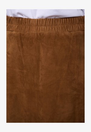Brown suede skirt with elastic waistband worn over a white top, showing texture and stitching details.