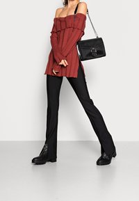Red ribbed off-shoulder top with layered ruffles, paired with black fitted pants and chunky black platform boots. Black textured handbag with chain strap.
