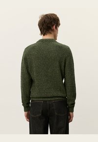 Suéter de punto verde con un acabado texturizado, cuello redondo y puños y dobladillo acanalados, combinado con unos jeans de mezclilla oscura. Vista trasera mostrada.