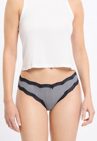 Biancheria intima stile bikini a righe bianche e nere con rifiniture in pizzo, caratterizzata da un piccolo fiocco al centro e una morbida texture in cotone.