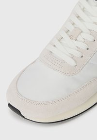 Sneaker met een combinatie van lichtgrijs suède en wit synthetisch materiaal, ronde neusdesign en platte witte veters.