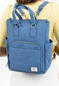 Blue ribbed backpack with double handles, adjustable straps, front zip pocket, and side pockets. Material appears smooth with a slight sheen.