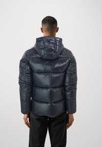 Marineblaue Steppjacke mit glänzender Optik, Kapuze und gestepptem Design, mit mittellangem Schnitt und elastischen Bündchen.