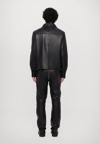 Black leather jacket with a collar, smooth texture, and straight cut, paired with fitted black leather pants and black boots.