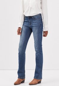Jeans rectos de un azul oscuro con una textura suave, cintura a media altura y un ligero desgastado, combinados con botas de tacón marrones hasta el tobillo.