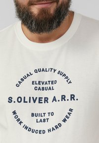 White cotton t-shirt featuring a circular graphic in navy blue text with phrases like "CASUAL QUALITY SUPPLY" and "BUILT TO LAST."