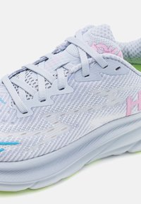 Scarpa da atletica azzurro chiaro con tomaia in rete, dettagli rosa e suola testurizzata. Presenta un collare imbottito, lacci piatti e un logo prominente.