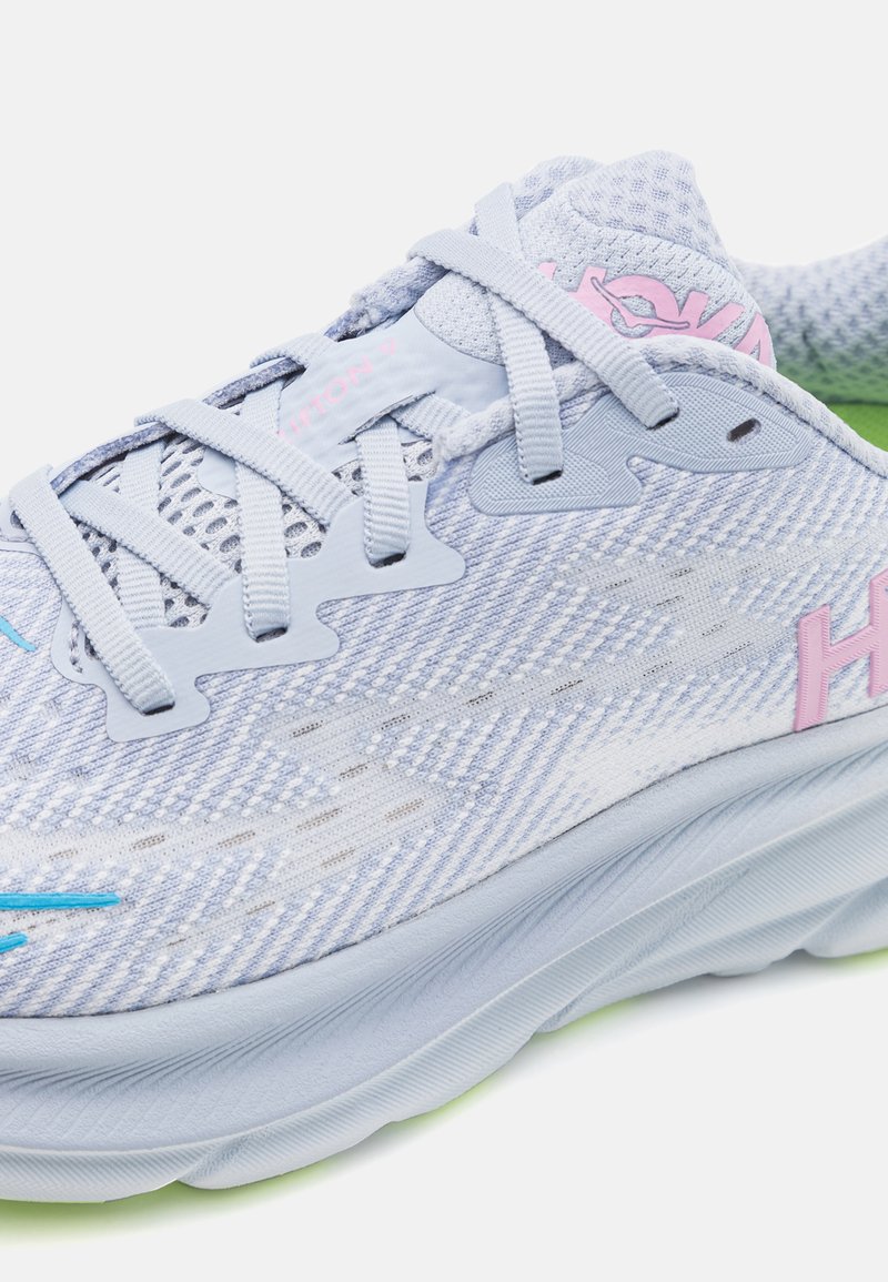 Hellblauer Sportschuh mit Mesh-Obermaterial, pinken Akzenten und strukturiertem Sohle. Verfügt über einen gepolsterten Schaft, flache Schnürsenkel und ein auffälliges Logo.