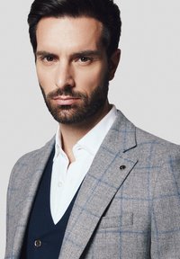 Szary, w kratkę, marynarka z klapą, połączona z granatowym kamizelką i białą koszulą. Posiada jeden guzik i subtelne niebieskie linie.