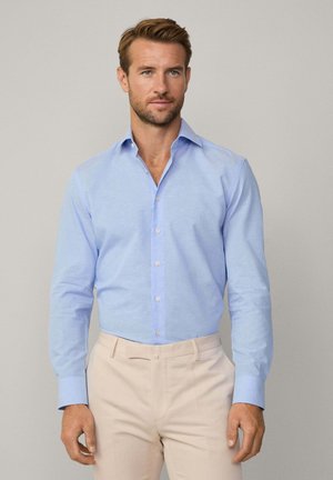 Light blue button-up shirt with a fine check pattern, long sleeves, and a spread collar; paired with light beige trousers.