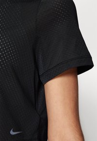 Musta Nike urheilupaita, jossa on teksturoitu, hengittävä muotoilu, lyhyet hihat ja pieni logo vasemmassa alareunassa.