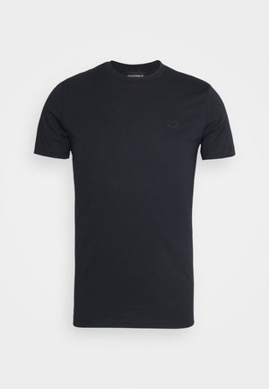 Camiseta negra lisa de manga corta con cuello redondo y un pequeño parche con un logo sutil en el pecho izquierdo sobre un fondo blanco.