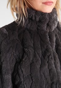 Grijze nepbontjas met een hoge kraag, voorzien van een gewatteerde textuur en een zachte afwerking, met een geweven patroon in donkere tinten.