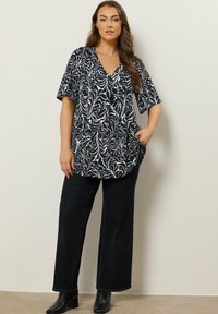 Navy blouse met een wit abstract golvenpatroon, korte mouwen, V-hals, zijkanten met zakken. Gecombineerd met zwarte wijde jeans en enkellaarsjes.