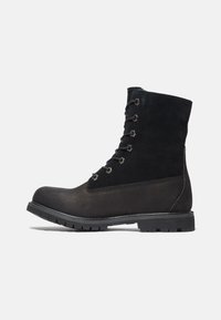 Botas de senderismo negras con una combinación de ante y cuero. Presentan un diseño con cordones, ojales metálicos y una suela de goma texturizada.