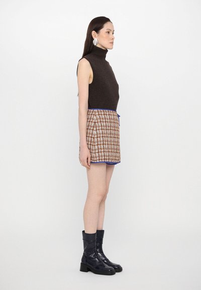 Brūns bez piedurknēm turtlenecks top, pārbaudīts brūns mini svārks ar zilu apdari un spīdīgi melni potītes zābaki ar bloku papēdi.
