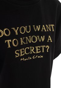 T-shirt en coton noir avec texte brodé doré : "VEUX-TU CONNAÎTRE UN SECRÉT ?" et "Manila Grace," avec un col arrondi.