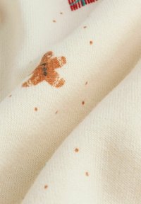 Warme crèmekleurige stof met een zachte textuur, voorzien van een pepperman-motief en verspreide lichtbruine spikkels. Gezellige en gestructureerde brei-design.
