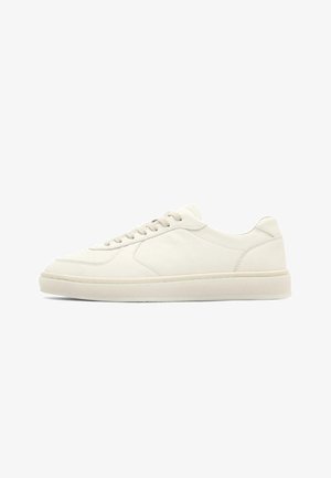 Nízký teniskový model z krémově bílé kůže s předním šněrováním a plochou gumovou podrážkou, zobrazený z boku na bílém pozadí.