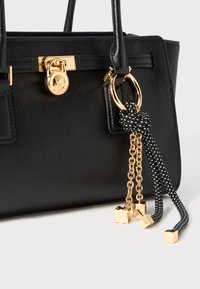 Black textured leather handbag with gold lock and decorative gold chains and black rope tassels with gold tips attached to handle.
