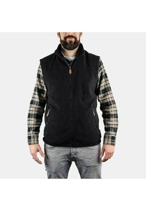 Gilet in pile nero con colletto alto, chiusura con zip e due tasche laterali. Indossato sopra una camicia a maniche lunghe a quadretti con tonalità di verde e beige.