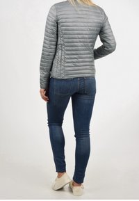 Jasnoszara, pikowana kurtka z poziomymi liniami, zestawiona z ciemnoniebieskimi jeansami slim fit i jasnymi butami, widok z tyłu.