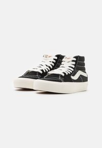 Zapatillas altas negras de ante, con cordones blancos, franja lateral en contraste y suelas de goma con detalles de costura visibles.