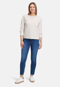Gestreiftes Langarmshirt in Creme und Hellbraun, kombiniert mit eng anliegenden blauen Jeans und weißen Sneakern. Lockere Passform, Bootsausschnitt.