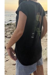 Černé tričko s květinovým potiskem na zadní straně a textem "LÁSKA A RŮŽE", krátké rukávy a kulatý lem. Nosené s denimovými šortkami.