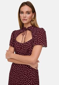 Bordeauxrotes Kleid mit gemustertem Design mit kleinen Sternen, kurzen Puffärmeln und einem Schlüsselloch-Ausschnitt mit Bindeband.