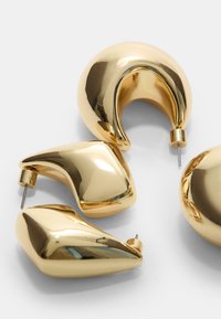 Boucles d'oreilles en or avec des formes organiques : un anneau lisse et arrondi, un design courbé, et une pièce angulaire élégante avec des finitions polies.