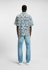 Lyhythihainen paita, jossa on sinisiä ja beigen värisiä kukkakuoseja, rento mitoitus. Yhdistetty vaaleansiinisiin farkkuihin ja valkoisiin lenkkareihin.