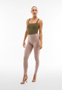 Body senza maniche verde oliva abbinato a leggings rosa chiaro a vita alta, caratterizzati da una texture liscia e un design aderente. Sandali con tacco trasparenti.