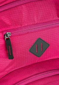 Zaino di colore rosa acceso realizzato in tessuto con superficie testurizzata, caratterizzato da un accento nero a forma di diamante e dettagli in cerniera argentata.