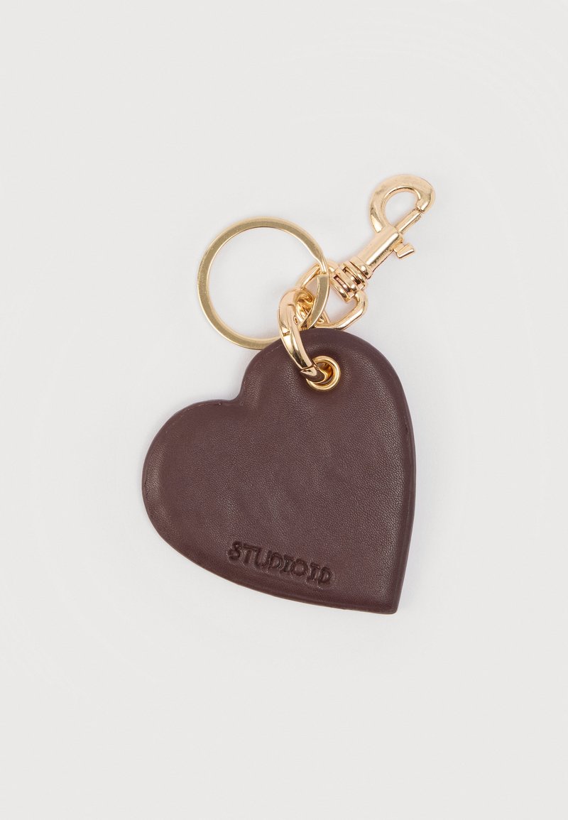 Μπρελόκ σε σχήμα καρδιάς, κατασκευ ασμένο από καφέ δέρμα με ομαλή υφή. Διαθέτει χρυσό μεταλλικό κούμπωμα και χαραγμένο λογότυπο.