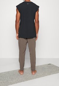 Sort ærmeløs sportstop med afrundede kanter, parret med løstsiddende beige bukser. Blød tekstur, minimal branding på bagsiden.