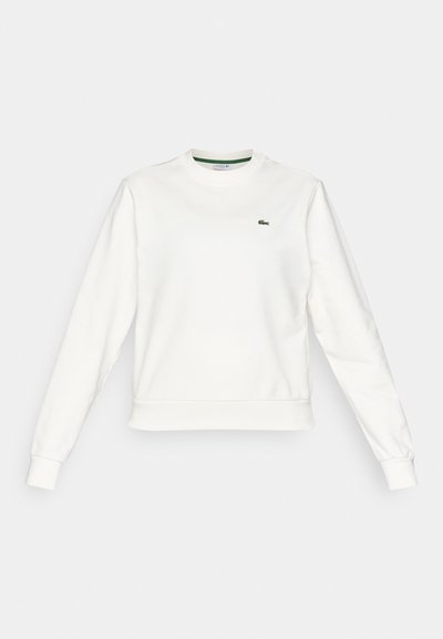 Sweatshirt blanc à col rond avec manches longues, poignets et ourlet côtelés, arborant un petit logo de crocodile vert sur la poitrine gauche.