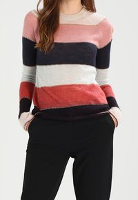 Gestreepte trui in tinten van roze, marineblauw en rood, met een ronde hals en een zachte textuur. Zwarte broek maakt de outfit compleet.