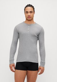 Cămașă henley gri cu mânecă lungă, cu textură ribbită, placket cu trei nasturi și design ajustat. Purtați-o cu pantaloni scurți negri.