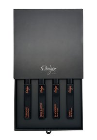 Schwarze Box mit vier rechteckigen schwarzen Fläschchen, beschriftet mit "TUBEROSE", "FEIGE & LOTUS", "BROMBEERE" und "TONKA". Elegantes Design mit orangefarbener Schrift.