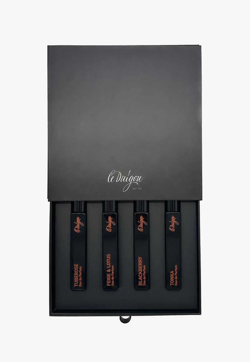 Schwarze Box mit vier rechteckigen schwarzen Fläschchen, beschriftet mit "TUBEROSE", "FEIGE & LOTUS", "BROMBEERE" und "TONKA". Elegantes Design mit orangefarbener Schrift.