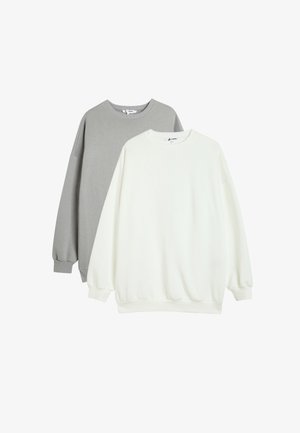 Deux sweatshirts empilés. L'un est gris clair, l'autre est blanc. Les deux présentent des poignets côtelés, un col rond et une coupe décontractée.
