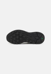 Black rubber sole with multi-directional tread pattern, featuring a textured finish and green accent at heel. Durable and functional design.