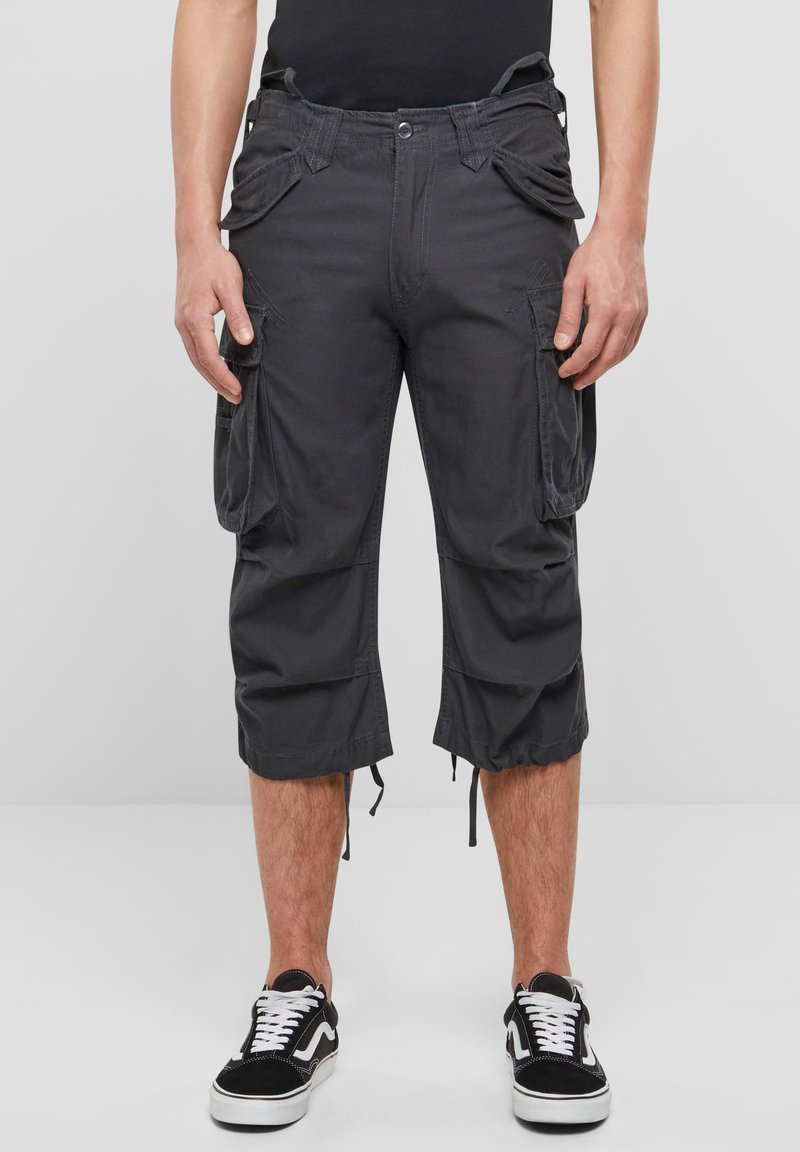 Tummanharmaat cargo-shortsit sivutaskuilla, säädettävillä nyörireunuksilla ja napillisesti suljettavat, yhdistettynä mustavalkoisiin lenkkareihin.