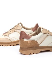 Baskets en cuir beige et blanc avec des accents en daim marron, présentant une semelle extérieure texturée et un design à lacets. Marque Pikolinos visible.