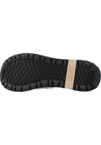 Suola di scarpa nera in gomma con superficie testurizzata e modellata; presenta un'etichetta del marchio beige. Battistrada prominente per aderenza e durata.