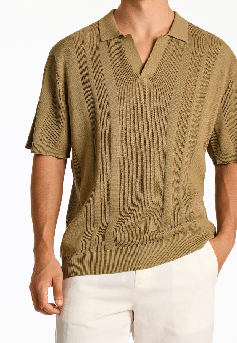 kortärmad olivgrön pikétröja med V-ringning, som har vertikal ribbad textur och subtila horisontella ränder, tillverkad av stickad tyg.