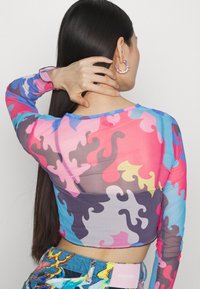 Langärmliges, kurzes Oberteil aus durchsichtiger Stoff mit mehrfarbigen, abstrakten Spiralmustern in Pink, Blau, Lila und Gelb.