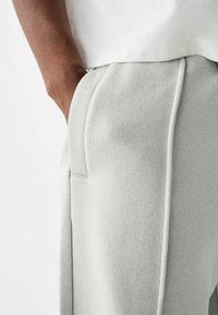 Light grey sweatpants featuring a textured fabric, side pocket, and contrasting piping along the seams for added detail.